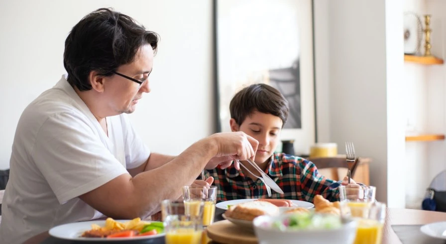 A child joyfully eating a meal with his dad, highlighting the importance of nutrition and paternal care.