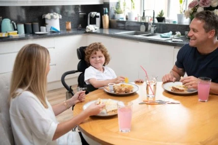 A child in a wheelchair enjoying a meal with their parents, emphasizing the significance of nutrition and family bonding.